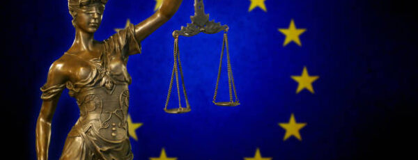 Close-up of a small bronze statuette of Lady Justice before the European Union flag.